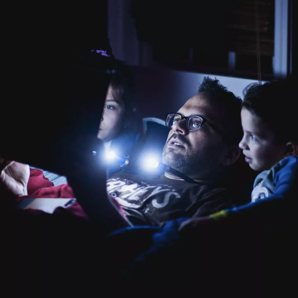 A father reading a bedtime story in the dark to his children.