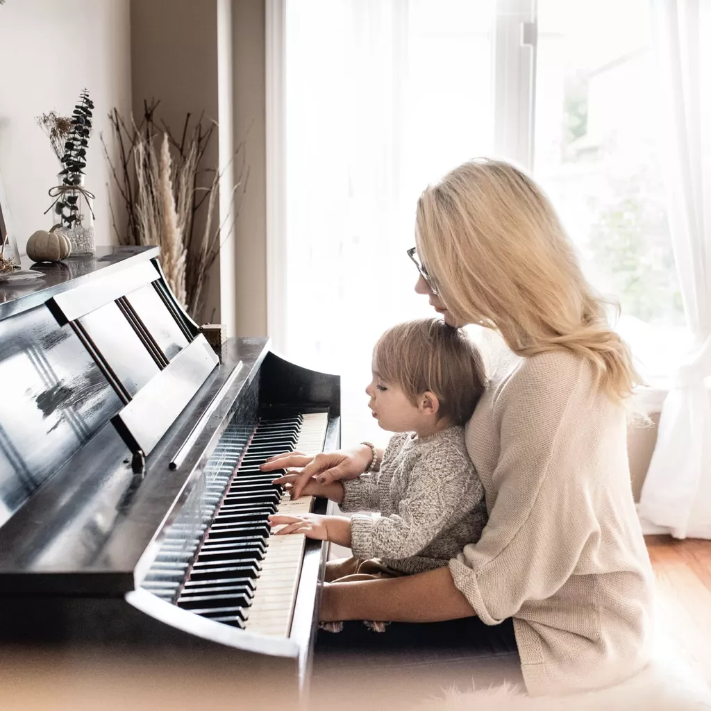 A mother teaching her daughter how to play the piano.