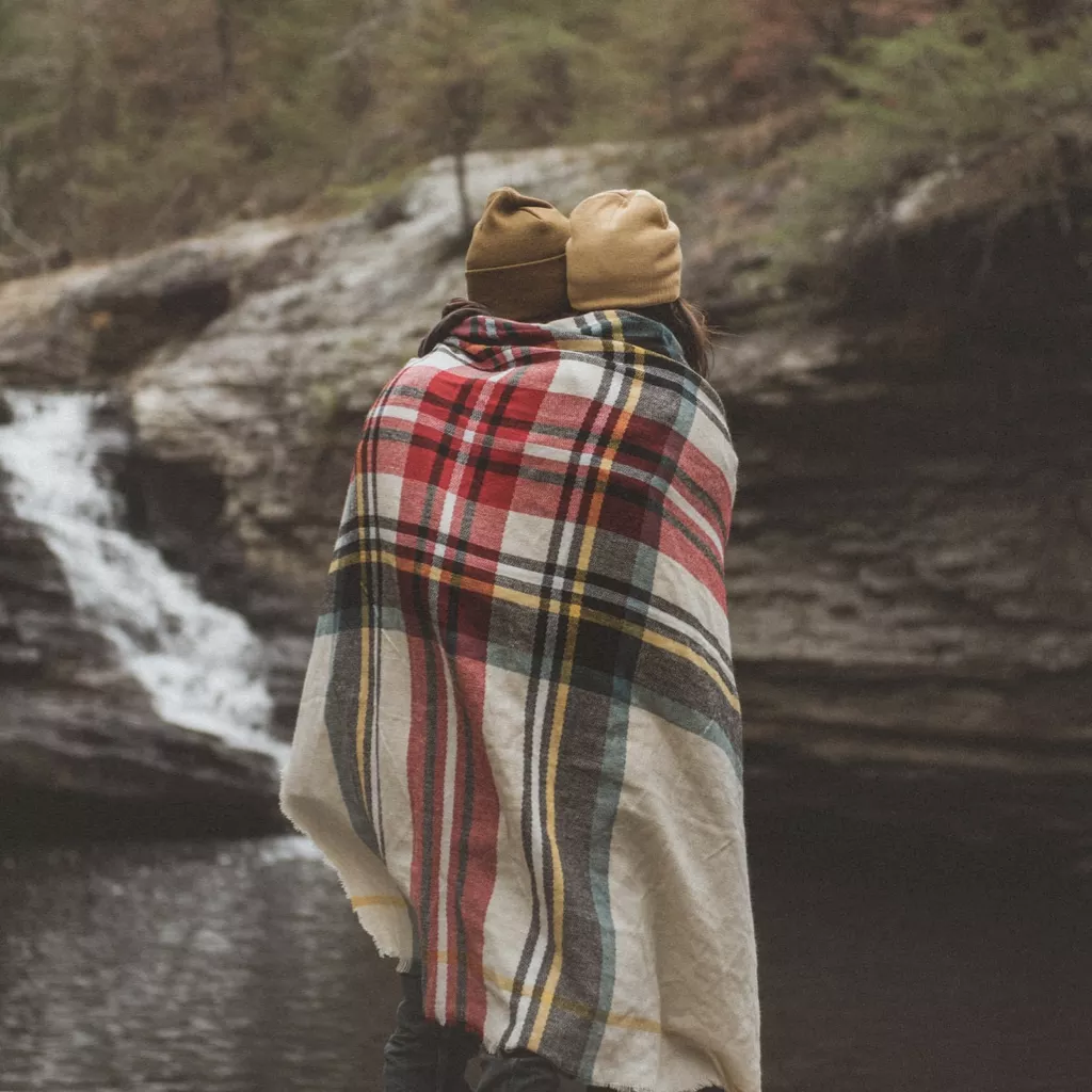 A mother and daughter sharing a blanket by a waterfall.