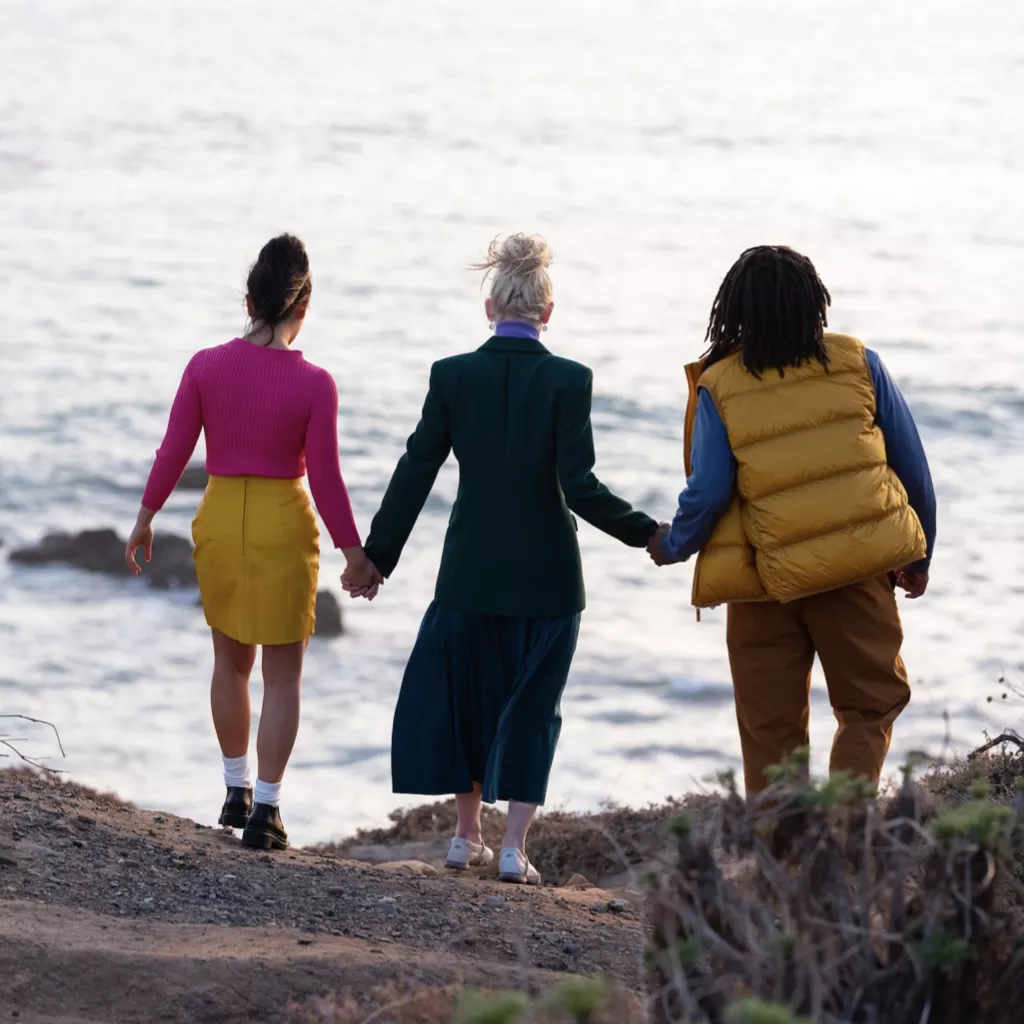 Three friends hand in hand look out to sea.