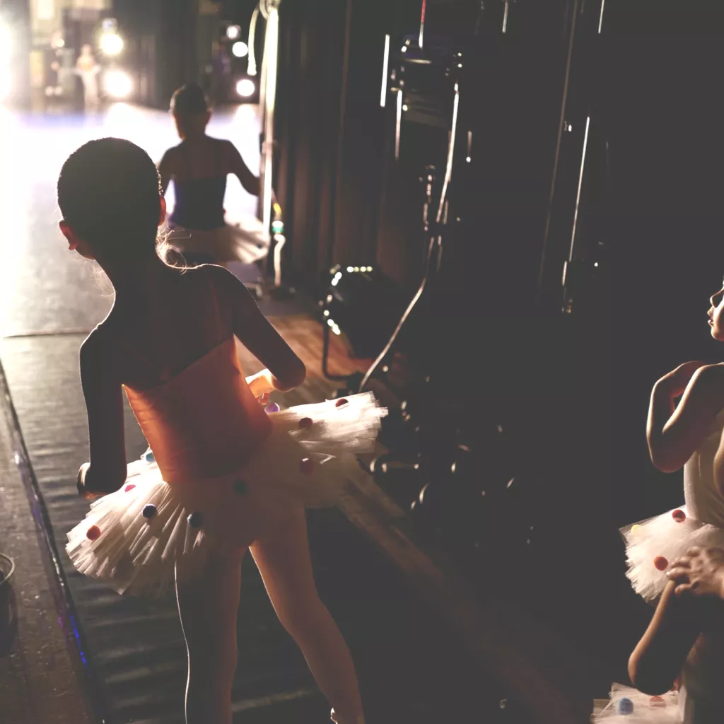 A young ballet dancer about to step out onto the stage.